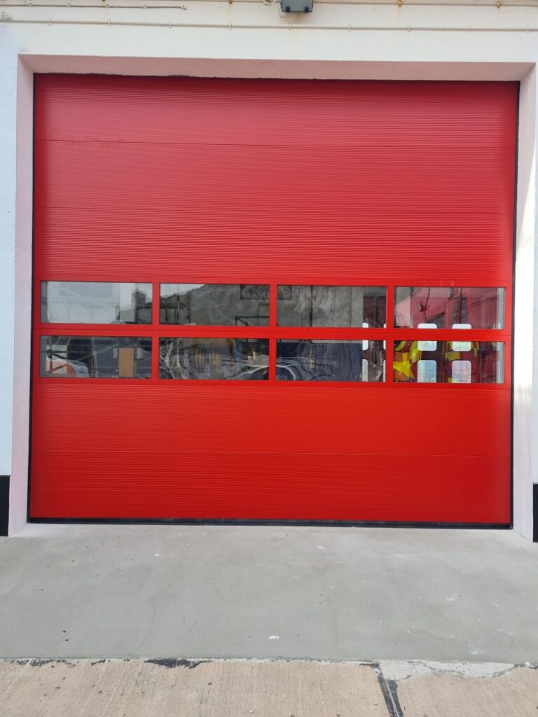 puerta roja enrollable vista desde el exterior de una nave, tiene aberturas horizontales que permiten la visión y el paso de la luz